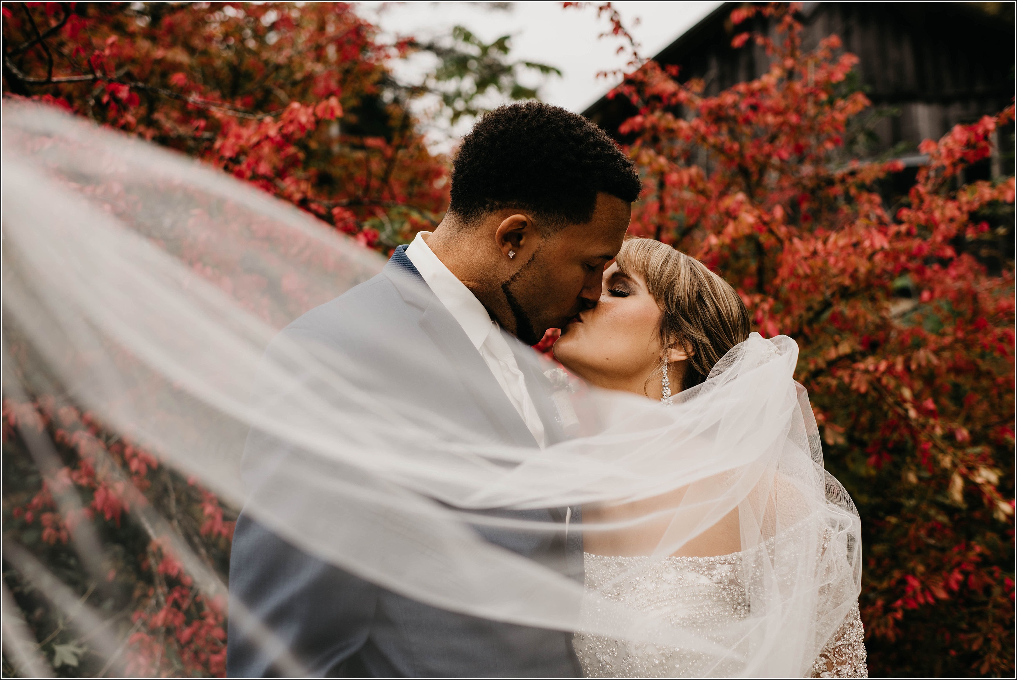 bride and groom kissing in front of beautiful red burning bush veil blowing in front romantic fall wedding