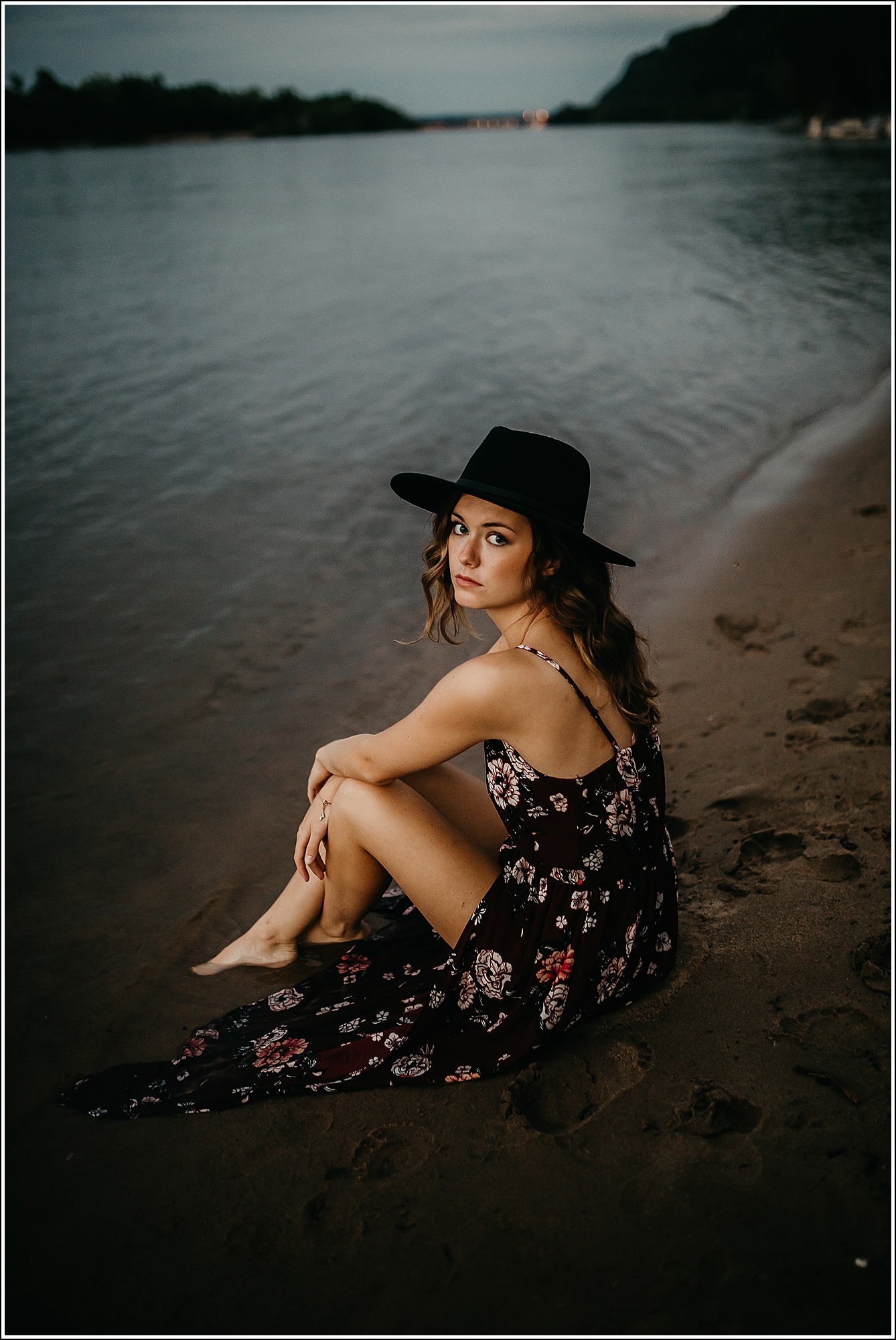 La Crosse WI senior photographer girl, floral dress flowers sitting in sand black hat beach water river lake